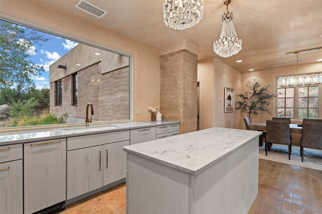 kitchen with a center island, sink, an inviting chandelier, decorative light fixtures, and light stone countertops