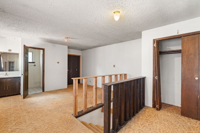 corridor with light carpet, a textured ceiling, and sink