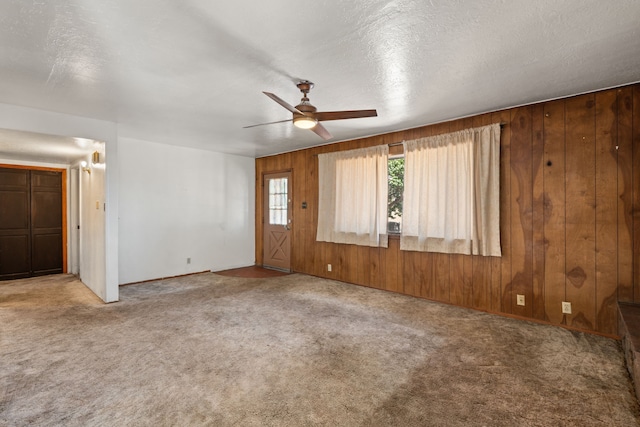 empty room featuring a textured ceiling, carpet, wood walls, and ceiling fan