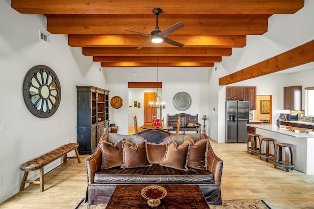 living area featuring light wood finished floors, visible vents, beamed ceiling, and ceiling fan with notable chandelier