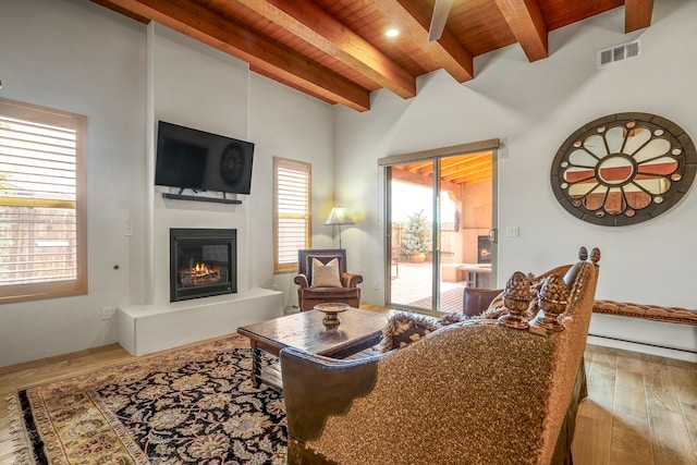 living room with visible vents, a glass covered fireplace, wood ceiling, beamed ceiling, and wood finished floors