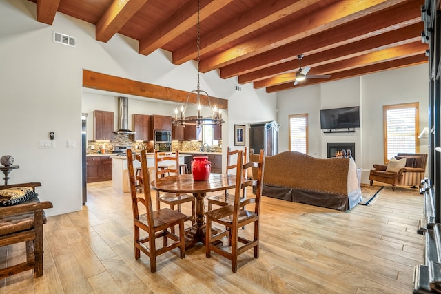 dining space with light hardwood / wood-style flooring, beam ceiling, and ceiling fan with notable chandelier