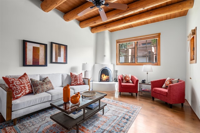 living room with ceiling fan, beamed ceiling, wood ceiling, hardwood / wood-style flooring, and a large fireplace