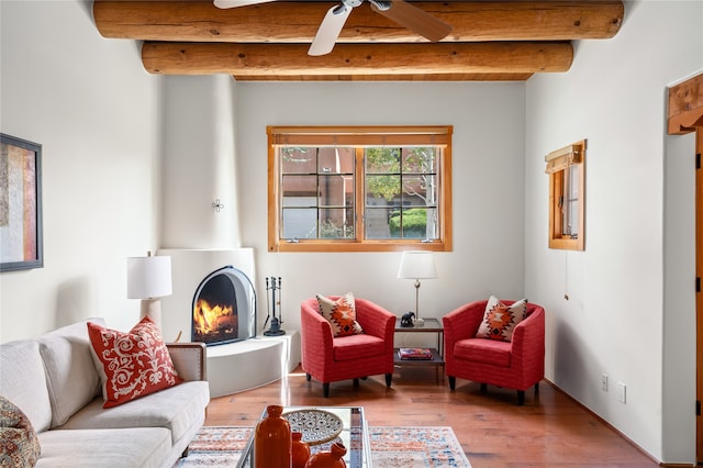 living room with ceiling fan, beam ceiling, wood-type flooring, and a large fireplace