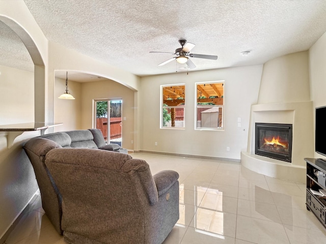 living room featuring light tile patterned floors, a fireplace, arched walkways, and ceiling fan