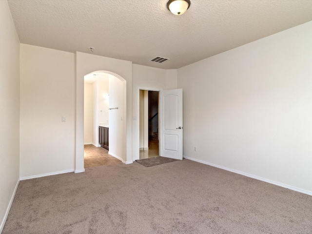 empty room featuring visible vents, arched walkways, baseboards, and carpet flooring