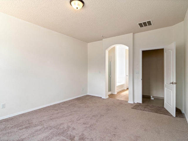 empty room featuring light carpet, baseboards, visible vents, arched walkways, and a textured ceiling