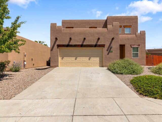 pueblo-style house with a garage, concrete driveway, fence, and stucco siding