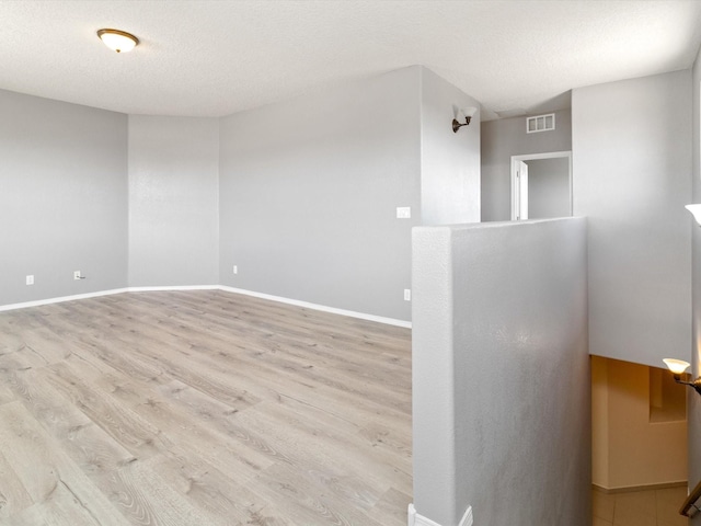 unfurnished room with a textured ceiling, wood finished floors, visible vents, and baseboards