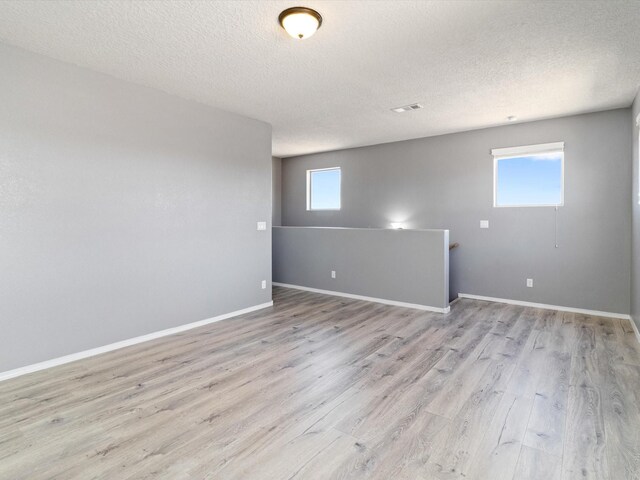 spare room with light wood finished floors, a textured ceiling, baseboards, and a wealth of natural light