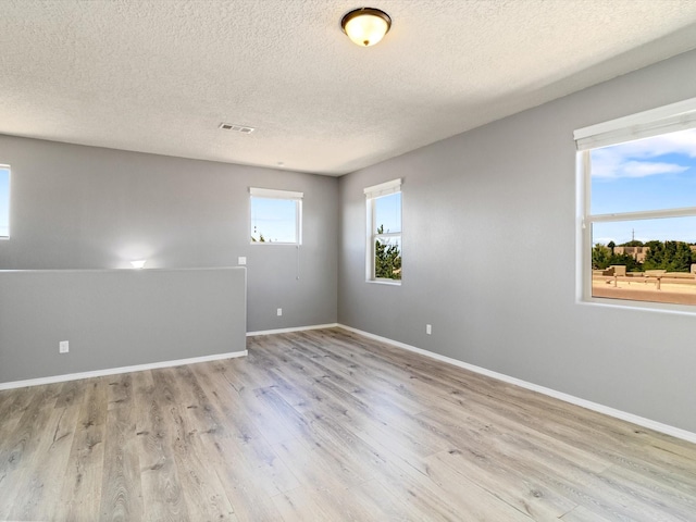 spare room with a textured ceiling, wood finished floors, visible vents, and baseboards