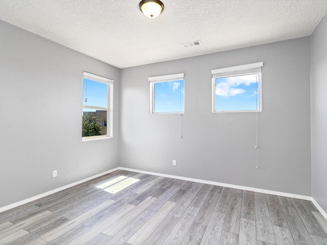 unfurnished room featuring visible vents, a textured ceiling, baseboards, and wood finished floors