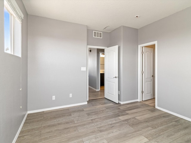 unfurnished bedroom with visible vents, light wood-type flooring, and baseboards