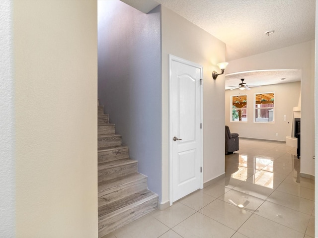 stairway with ceiling fan, a textured ceiling, baseboards, and tile patterned floors