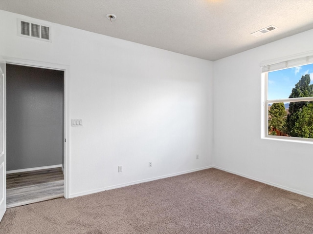 carpeted empty room with a textured ceiling, visible vents, and baseboards