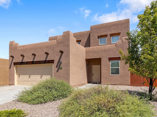 pueblo-style home with driveway, an attached garage, fence, and stucco siding