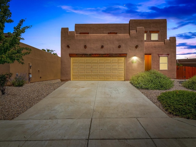 pueblo-style home with a garage, fence, concrete driveway, and stucco siding