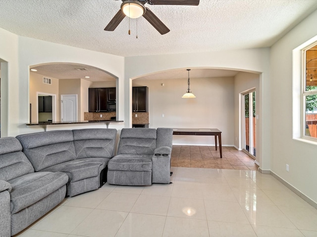 living room with light tile patterned floors, a ceiling fan, visible vents, arched walkways, and a textured ceiling