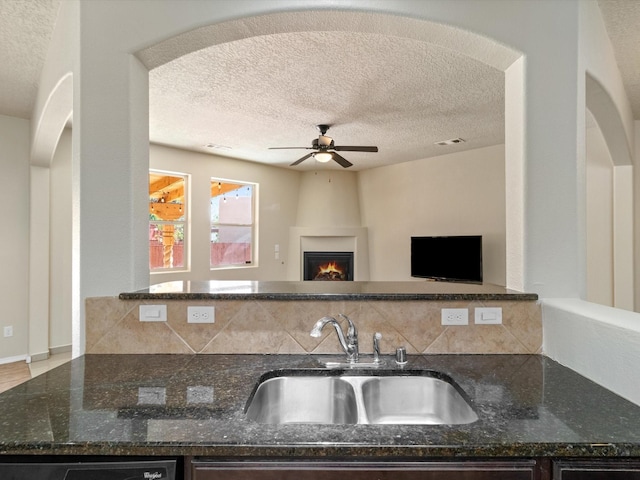 kitchen featuring visible vents, ceiling fan, dark stone countertops, a textured ceiling, and a sink