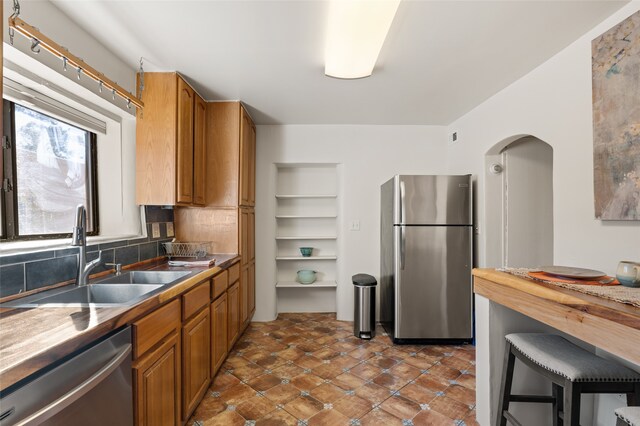 kitchen with stainless steel appliances, sink, tasteful backsplash, and wood counters