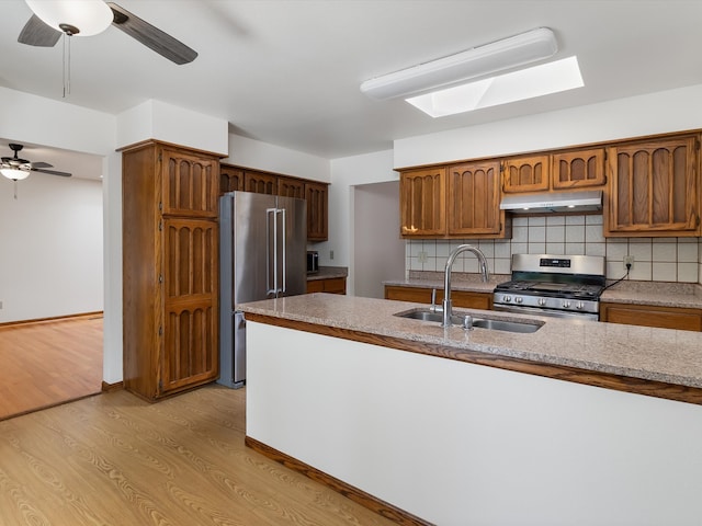 kitchen featuring decorative backsplash, a skylight, stainless steel appliances, sink, and light hardwood / wood-style flooring