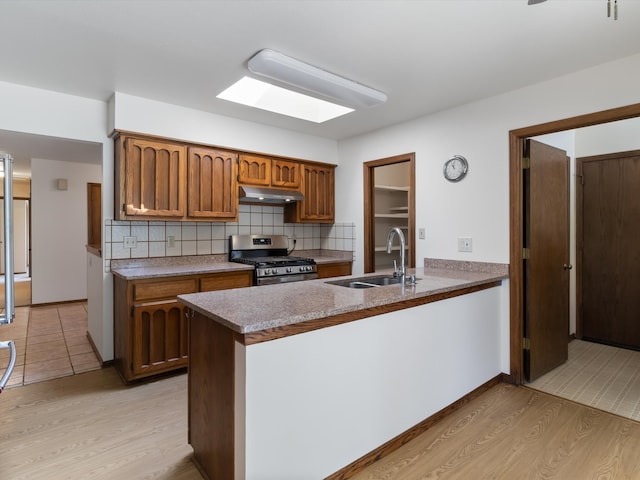 kitchen featuring kitchen peninsula, tasteful backsplash, stainless steel gas range, sink, and light hardwood / wood-style floors