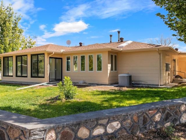 rear view of house with central AC unit and a lawn