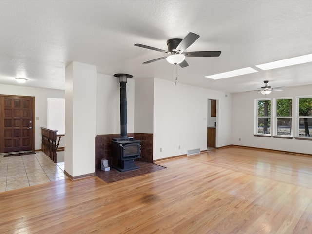 unfurnished living room featuring a textured ceiling, light hardwood / wood-style floors, a wood stove, and a skylight