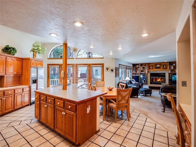 2176 La Tierra, Los Alamos, NM 87544 - kitchen with stainless steel fridge, a textured ceiling, tile countertops, light colored carpet, and a glass covered fireplace