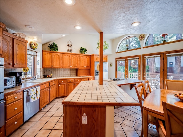 kitchen featuring a kitchen island, a textured ceiling, stainless steel appliances, tile countertops, and vaulted ceiling