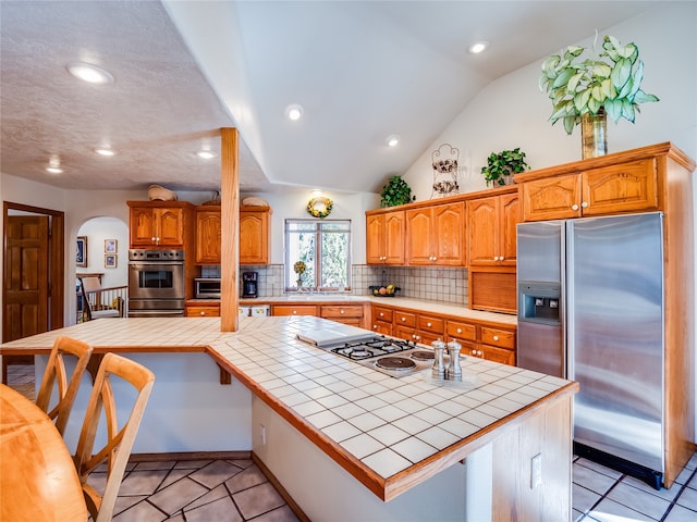 kitchen featuring appliances with stainless steel finishes, a kitchen island, vaulted ceiling, and tile countertops