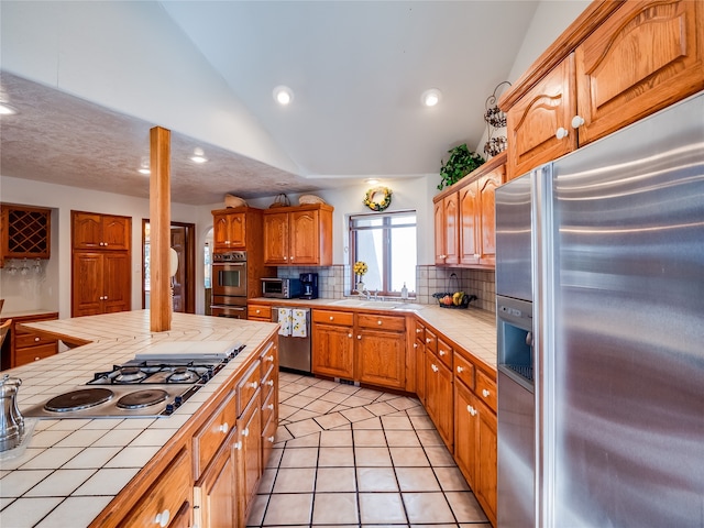 kitchen featuring lofted ceiling, stainless steel appliances, backsplash, tile countertops, and light tile patterned floors