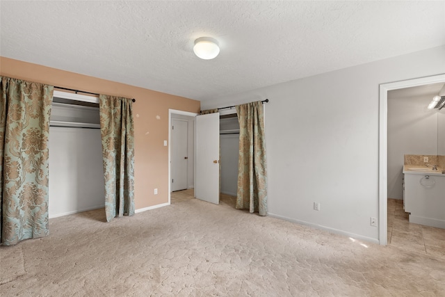 unfurnished bedroom featuring ensuite bath, a textured ceiling, light colored carpet, and sink