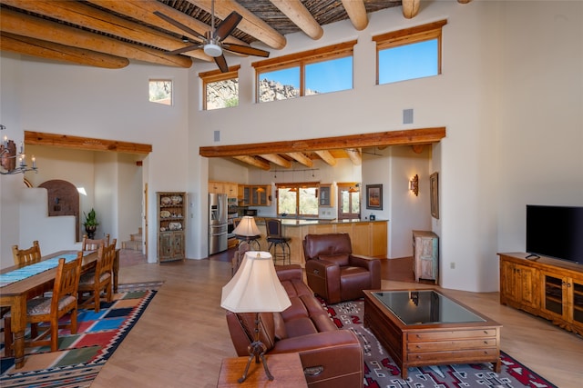 living room with ceiling fan, light hardwood / wood-style flooring, a towering ceiling, and beam ceiling