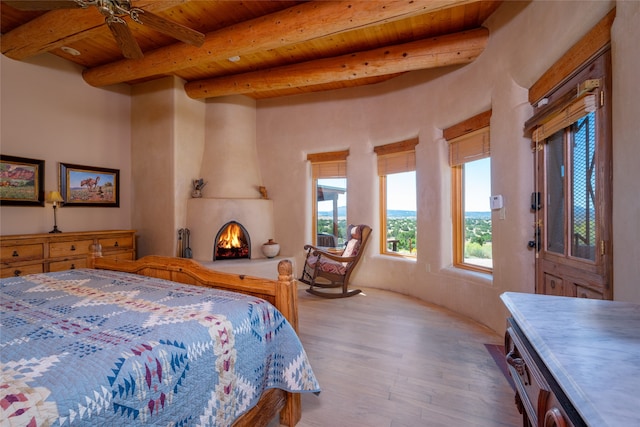 bedroom featuring light hardwood / wood-style floors, beamed ceiling, a fireplace, ceiling fan, and wooden ceiling