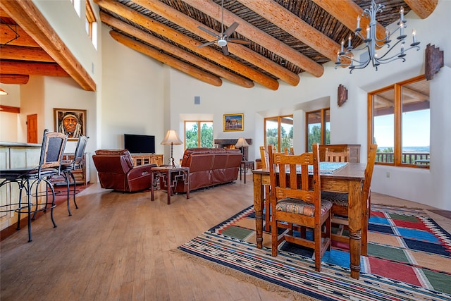 dining area with ceiling fan with notable chandelier, beam ceiling, a towering ceiling, and hardwood / wood-style flooring