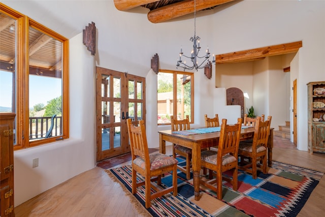 dining space featuring beamed ceiling, french doors, light hardwood / wood-style flooring, a high ceiling, and a notable chandelier