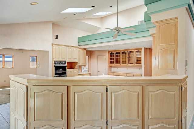 kitchen featuring cream cabinetry, a towering ceiling, oven, ceiling fan, and a skylight