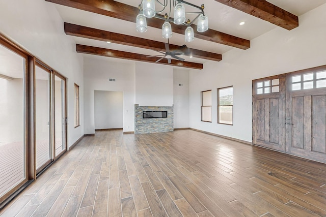 unfurnished living room with beamed ceiling, ceiling fan with notable chandelier, and a fireplace