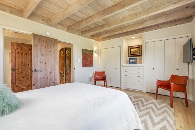 bedroom featuring beam ceiling, light wood-type flooring, wood ceiling, and two closets