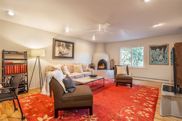 living room featuring baseboard heating, ceiling fan, a fireplace, and hardwood / wood-style flooring