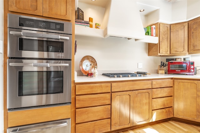 kitchen with stainless steel appliances, range hood, and light hardwood / wood-style floors