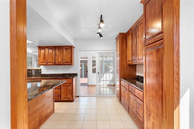 kitchen featuring light tile patterned flooring, dark stone counters, a textured ceiling, and rail lighting