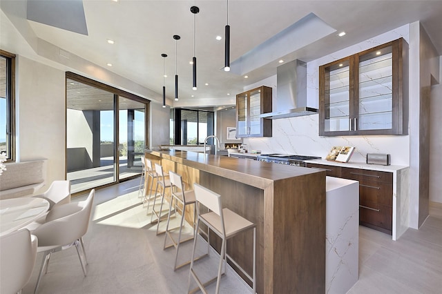 kitchen with decorative backsplash, pendant lighting, wall chimney exhaust hood, and a large island