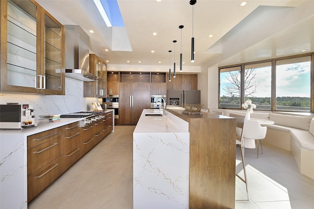 kitchen with light stone counters, stainless steel appliances, sink, a large island with sink, and decorative light fixtures