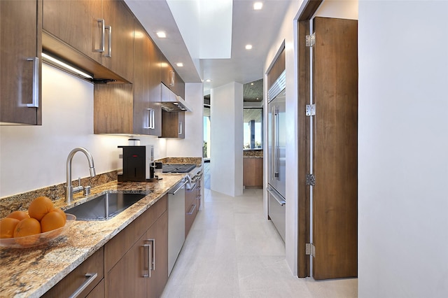 kitchen featuring a skylight, light stone countertops, sink, built in fridge, and range hood