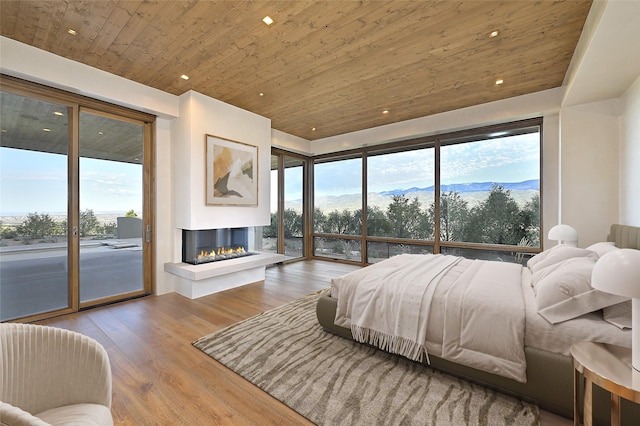 bedroom with wooden ceiling, a multi sided fireplace, light hardwood / wood-style flooring, a mountain view, and access to outside