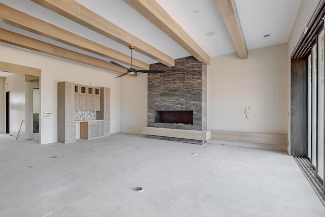 unfurnished living room featuring beam ceiling, ceiling fan, and a stone fireplace