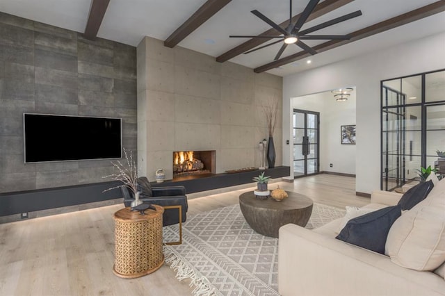 living room featuring wood-type flooring, a fireplace, beam ceiling, and ceiling fan