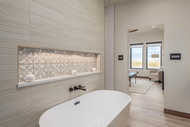 bathroom featuring tile walls, wood-type flooring, and a bathing tub